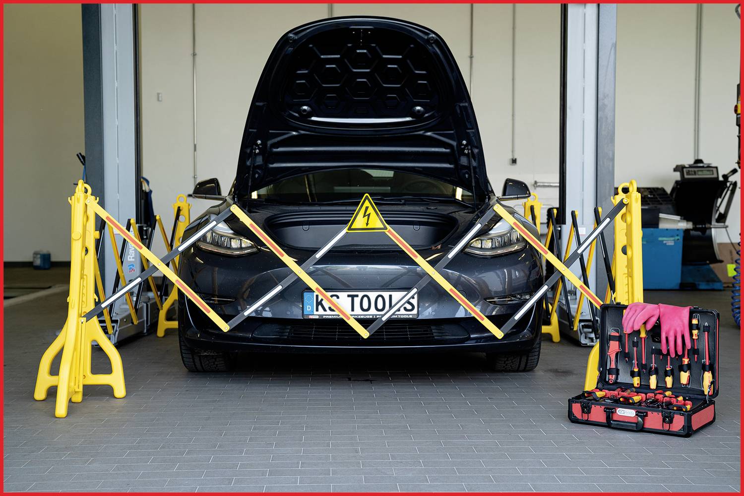 Automobil s otvorenim poklopcem motora stoji u radionici. Sigurnosne trake i znak upozorenja naznačuju električne radove održavanja.