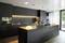 Moderna kuhinja s tamnim ormarićima, osvjetljenom radnom površinom i velikim kuhinjskim otokom. Veliki prozori s pogledom na vrt.