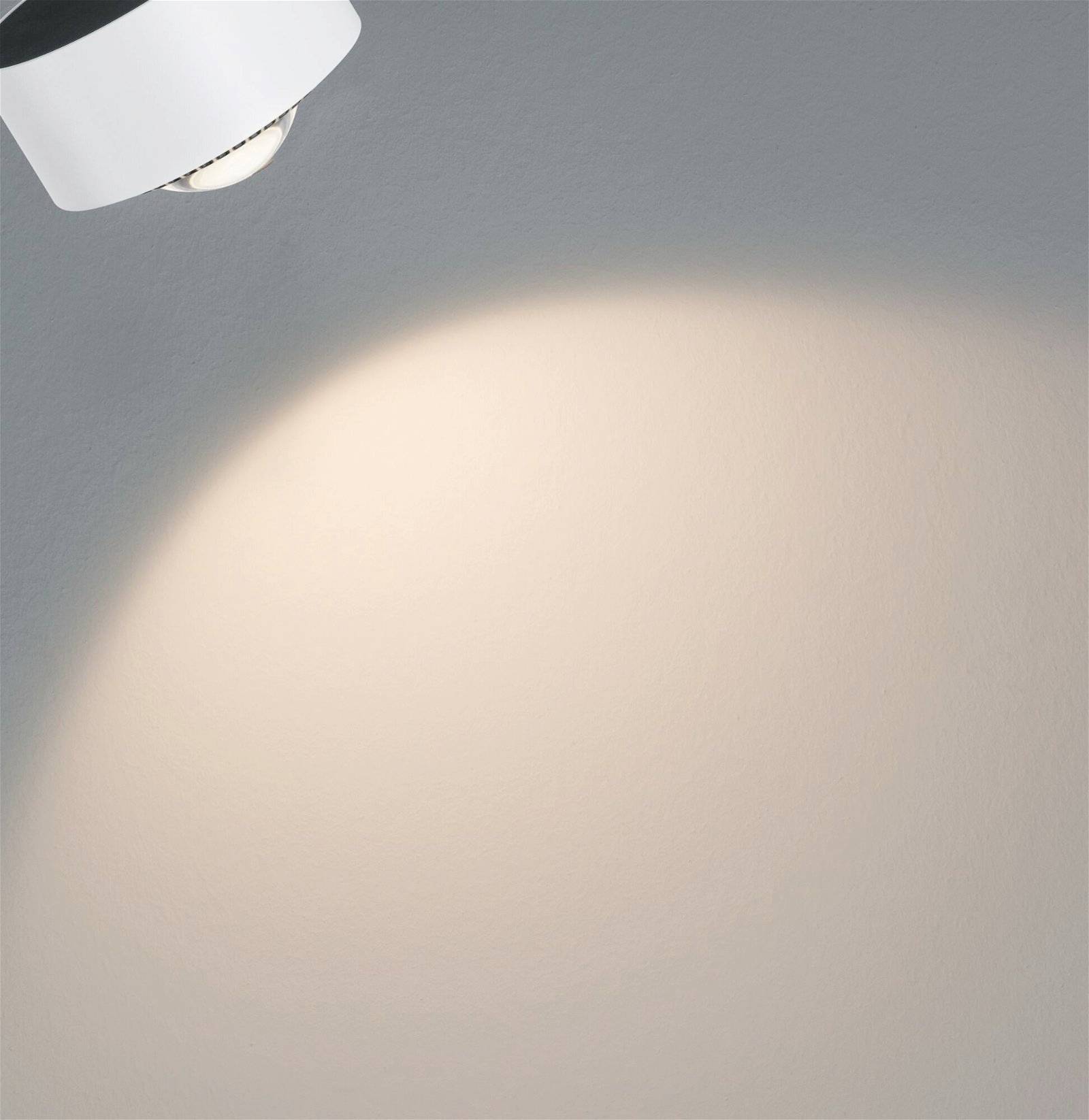 Lampa osvjetljava dio zida, stvarajući okrugli svjetlosni stožac na neutralnoj površini. Minimalistički dizajn.