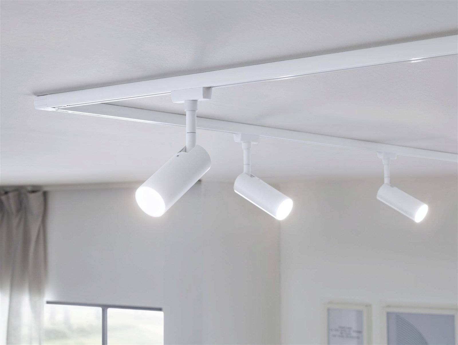 Moderna bijela stropna lampa s tri okretljiva cilindarska spots reflektora koji prostoriju osvjetljavaju toplim svjetlom.