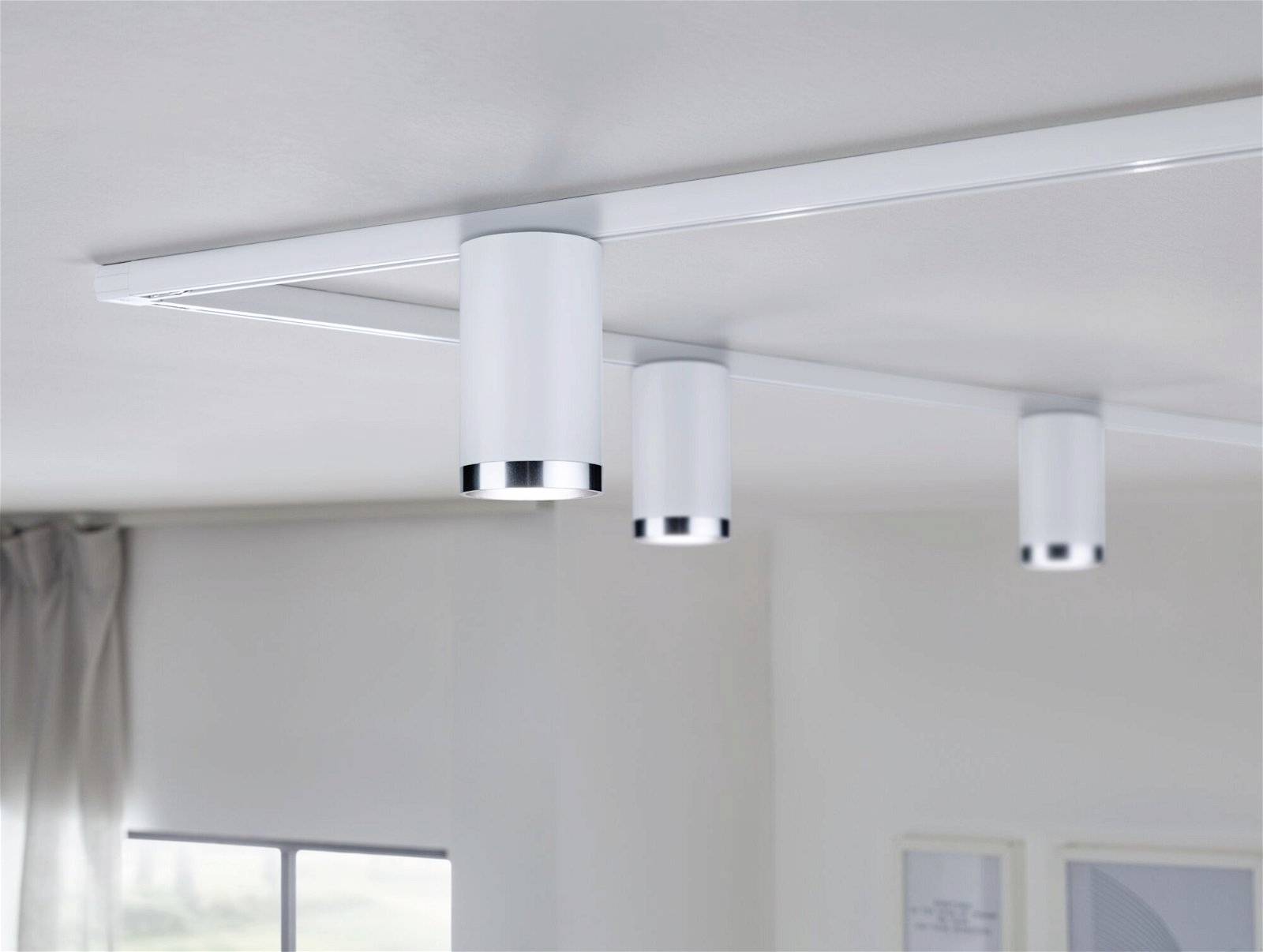 Tri bijele cilindrične stropne lampe montirane na šini osvjetljavaju prostoriju modernog uređenja dnevnom svjetlošću.