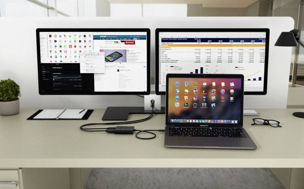 Radni stol s prijenosnim računalom povezanim na dva monitora. Monitori prikazuju web stranicu i tablicu.