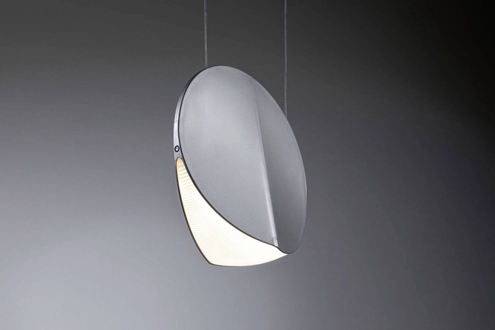 Moderna, okrugla viseća lampa s nagnutim metalnim štitom koji djelomično zaklanja svjetlo. Pozadina siva.