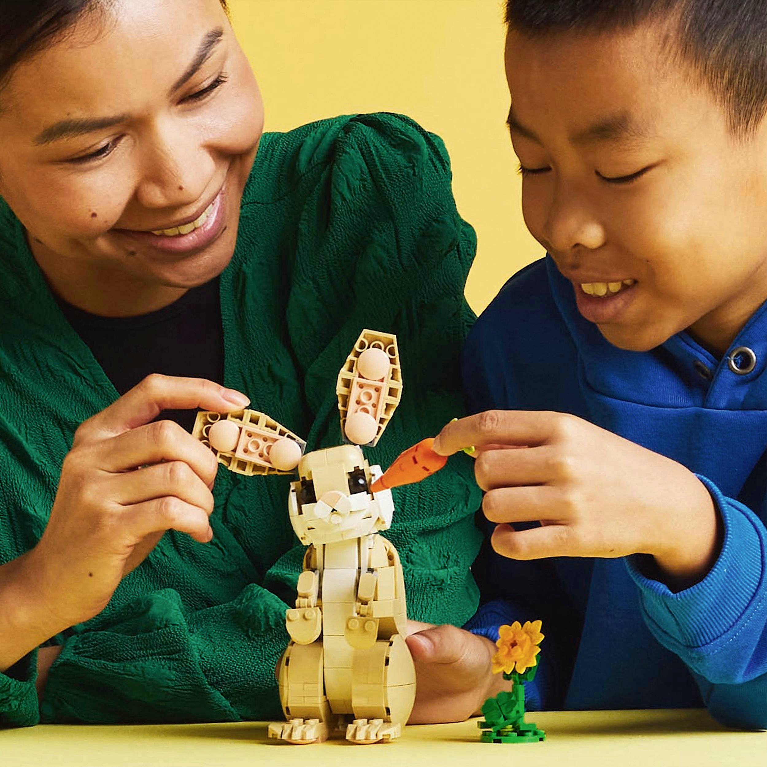Odrasla osoba i dijete se nasmješavaju dok zajedno grade Lego model zeca. Zec drži mrkvu, a pored njega se nalazi kreacija od cvijeća.