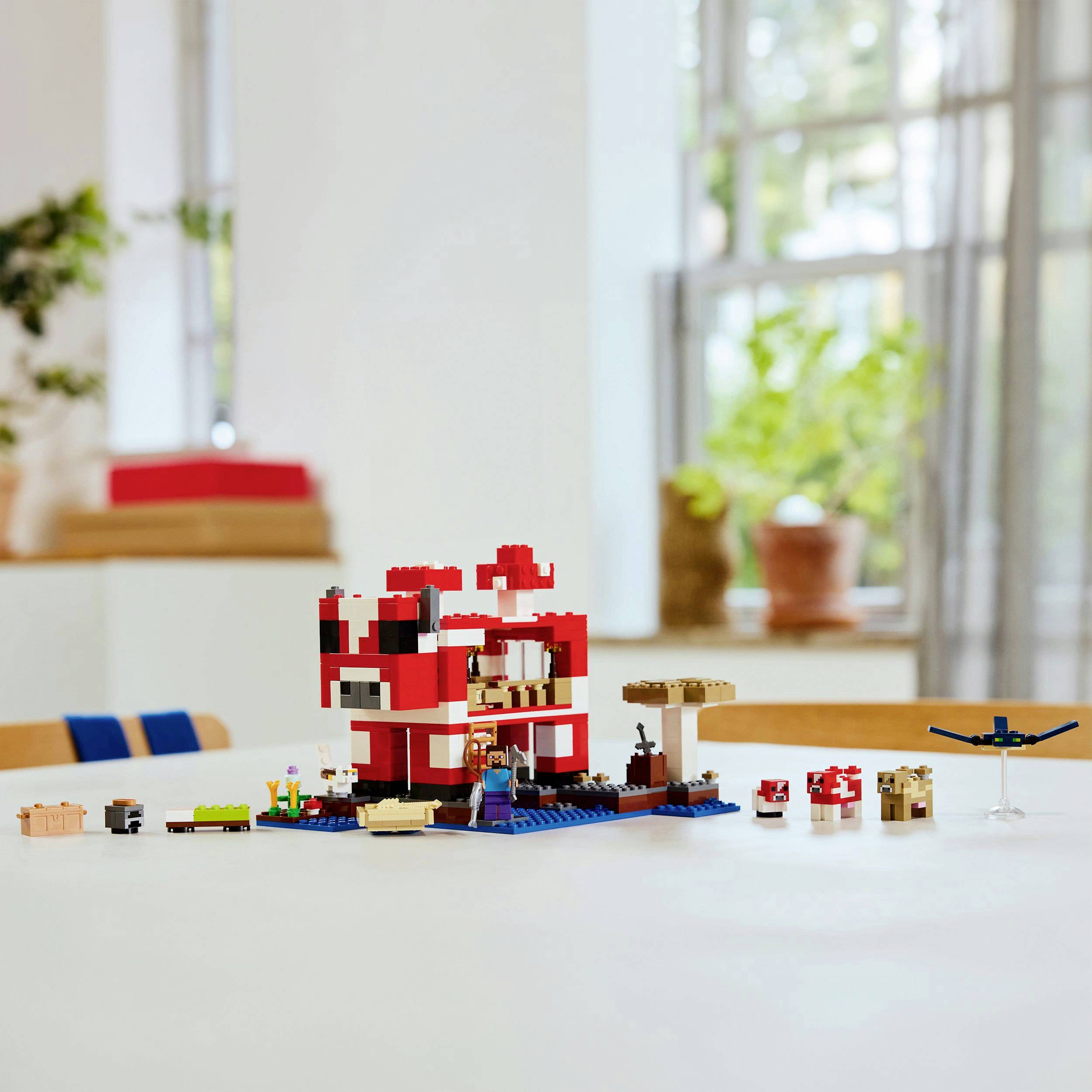 LEGO set gljive kuće stoji na stolu. Prikazuje crvenu i bijelu zgradu s okolnom vegetacijom i figurama.