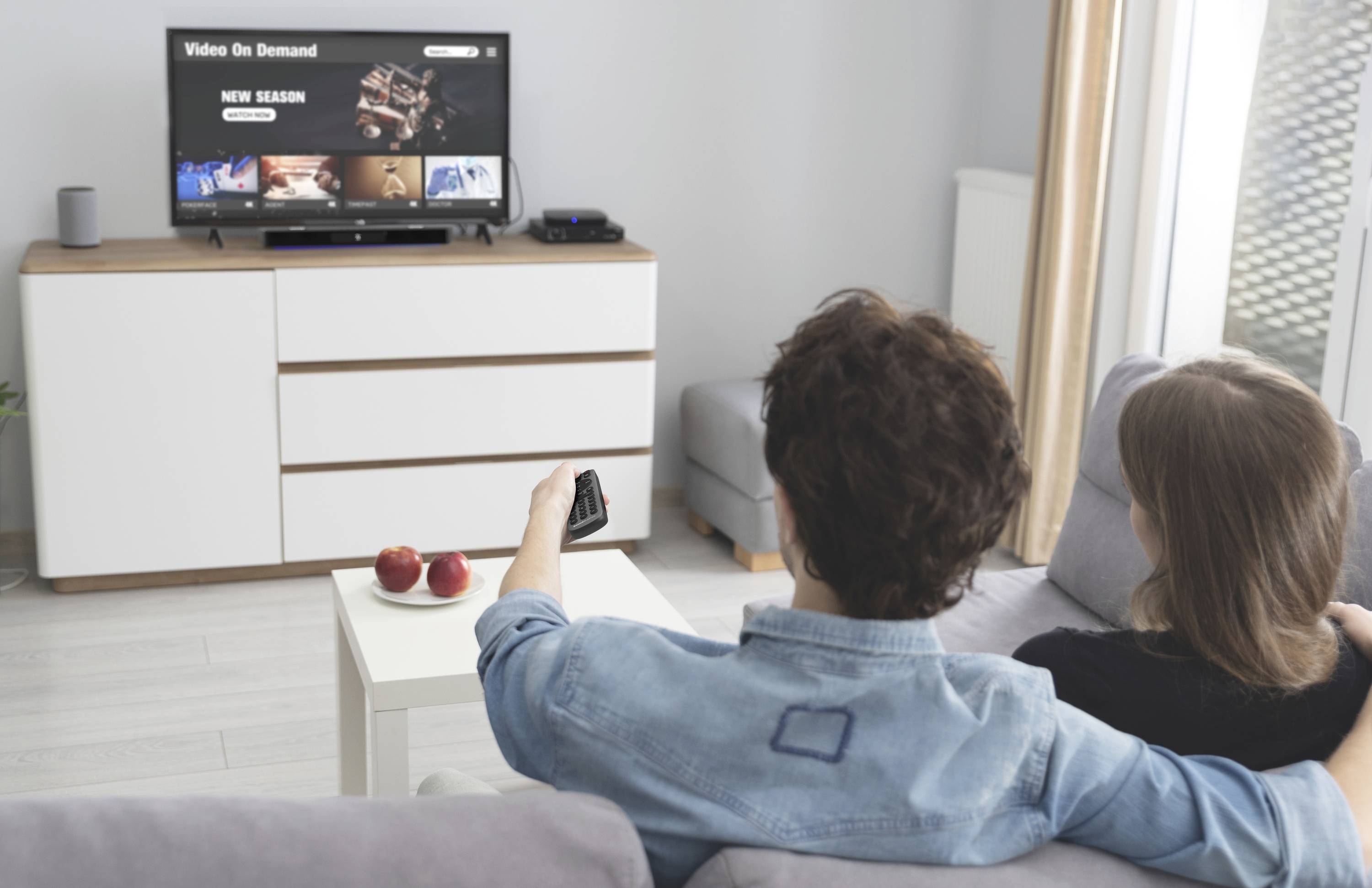 Par sjedi na kauču i gleda televiziju. Na ekranu je vidljiva opcija 'Video na zahtjev'.