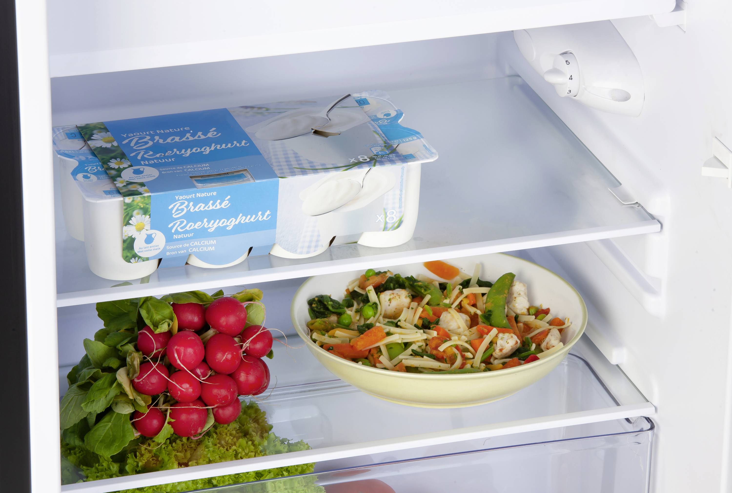 U hladnjaku: paket jogurta gore, ispod posuda sa salatom, ispod snopu rotkvica. Svježi i šareni izbor.