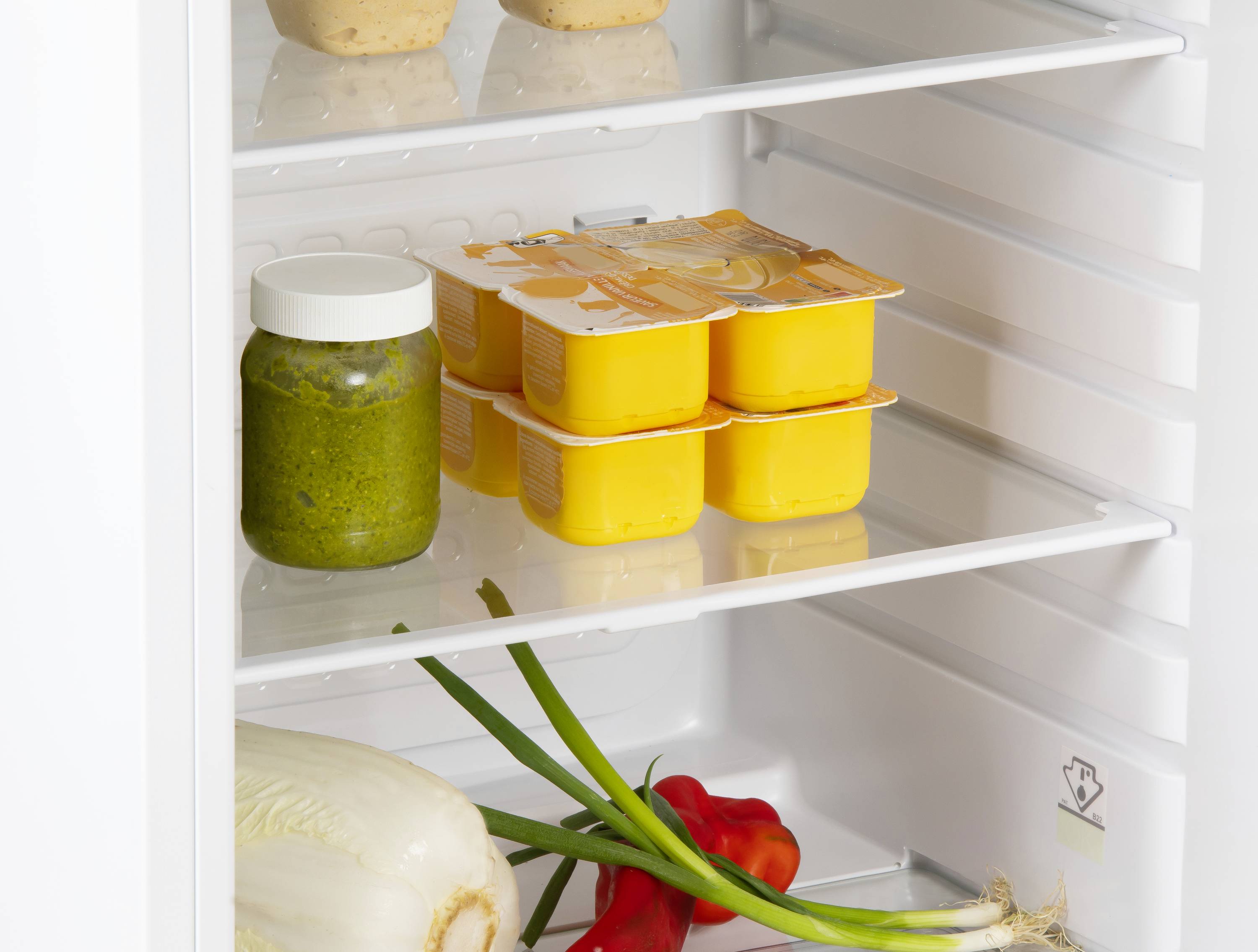 Otvoreni hladnjak prikazuje kruh gore, u sredini jogurt i staklenku pesta. Dolje leže mladi luk i paprika.