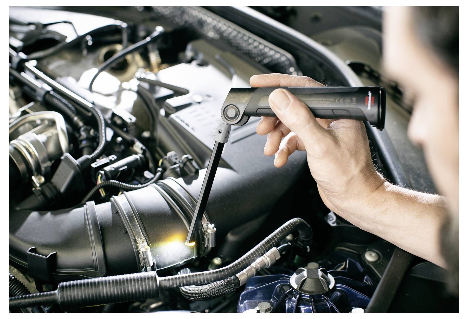 Mehaničar koristi baterijansku lampu kako bi pregledao i stegnuo vijak na automobilskom motoru ispod poklopca motornog prostora.