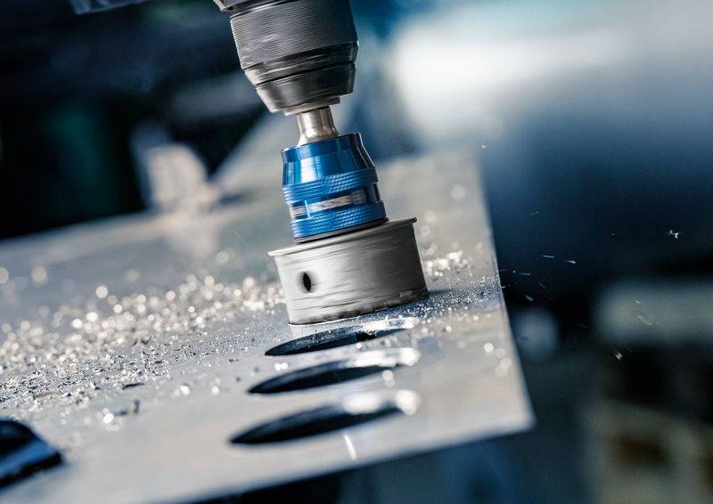 Bušilica pri bušenju rupe u metalnom limu, metalnu strugotine lete oko nje. Ovo prikazuje industrijski proizvodni proces.