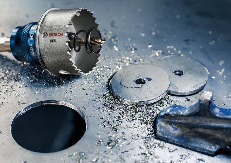 Bušna kruna Bosch leži na metalnoj podlozi pored rupa za bušenje i strugotina. Alat za bušenje u metalu.