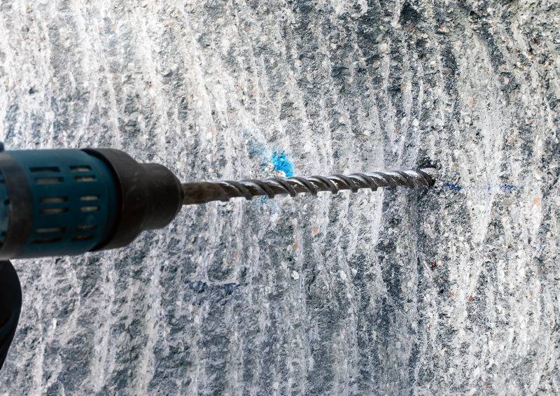 Borer buši rupu u sivoj, hrapavoj kamnoj površini.