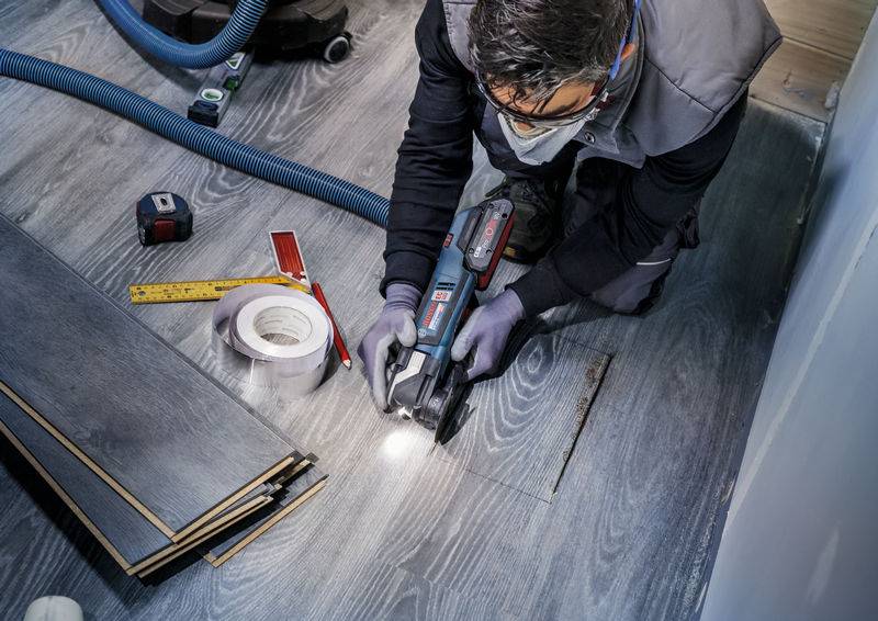 Osoba koja električnom pilom reže laminatni pod. Alati i materijali leže oko nje na podu.