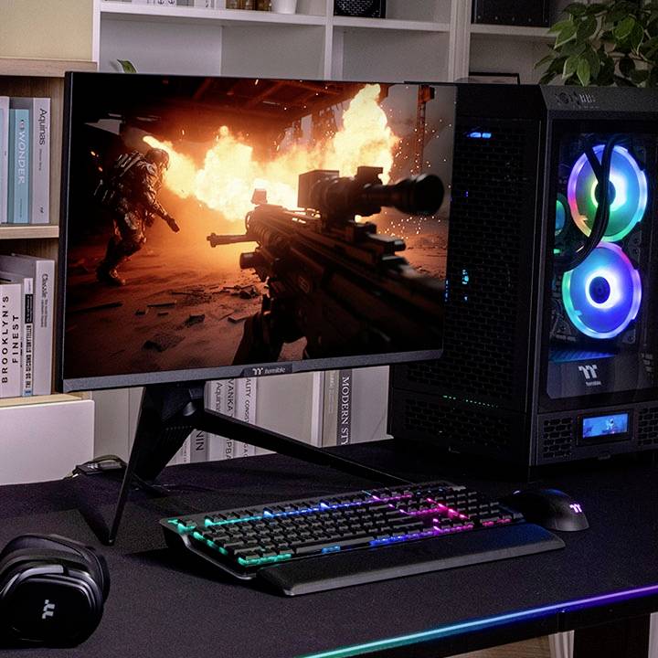 Radni stol s računalom koje prikazuje videoigru. Tipkovnica i miš s raznobojnim osvjetljenjem; PC ima prozirni bočni poklopac.
