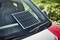 Solarni panel leži na prednjoj staklenoj površini crvenog automobila, očito za punjenje baterije pomoću sunčeve energije.