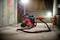 Crveni industrijski usisavač stoji u slabo osvijetljenoj podrumskoj prostoriji, osvjetljen gradilišnim reflektorima, pokraj kabela tipičnih za gradilište.