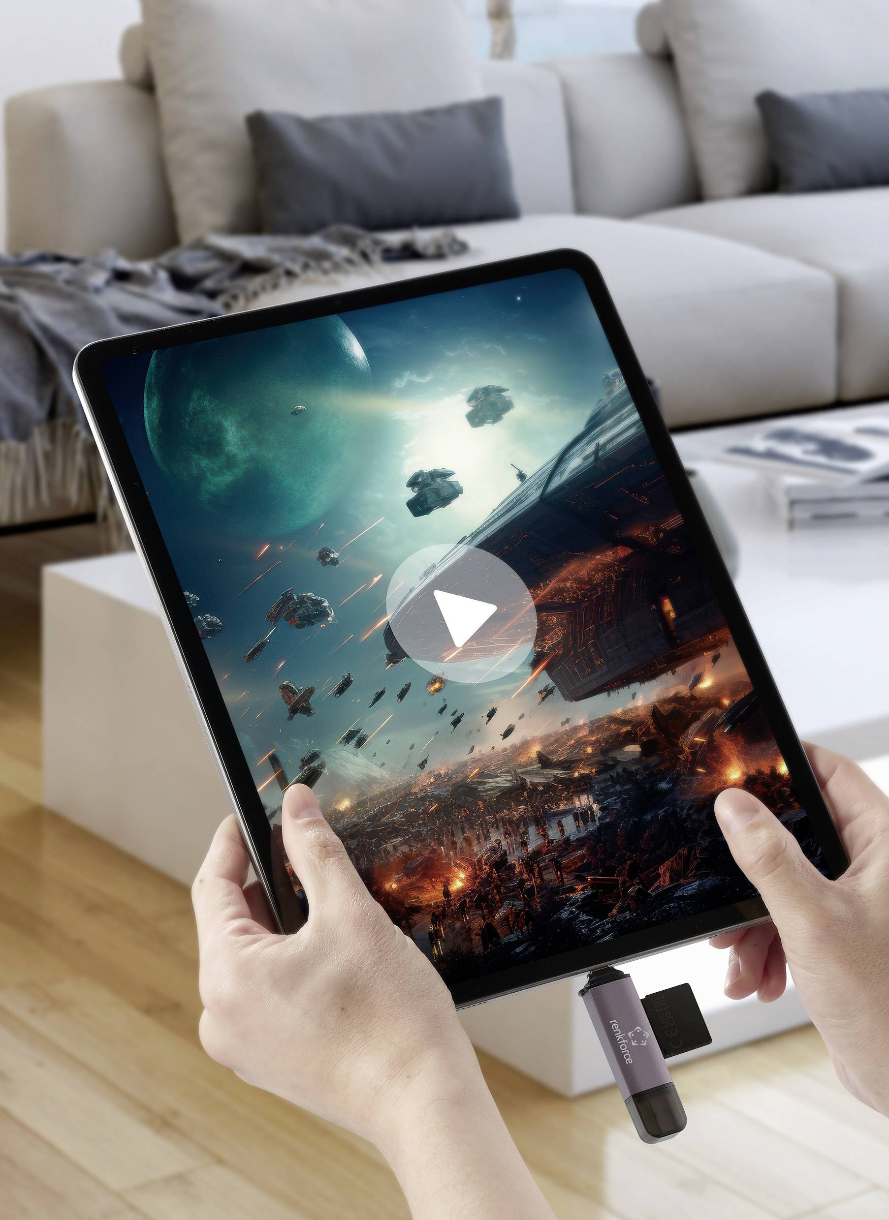 Tablet koji prikazuje svemirsku borilačku igru drže dvije ruke. U pozadini se vidi dnevna soba sa softom.
