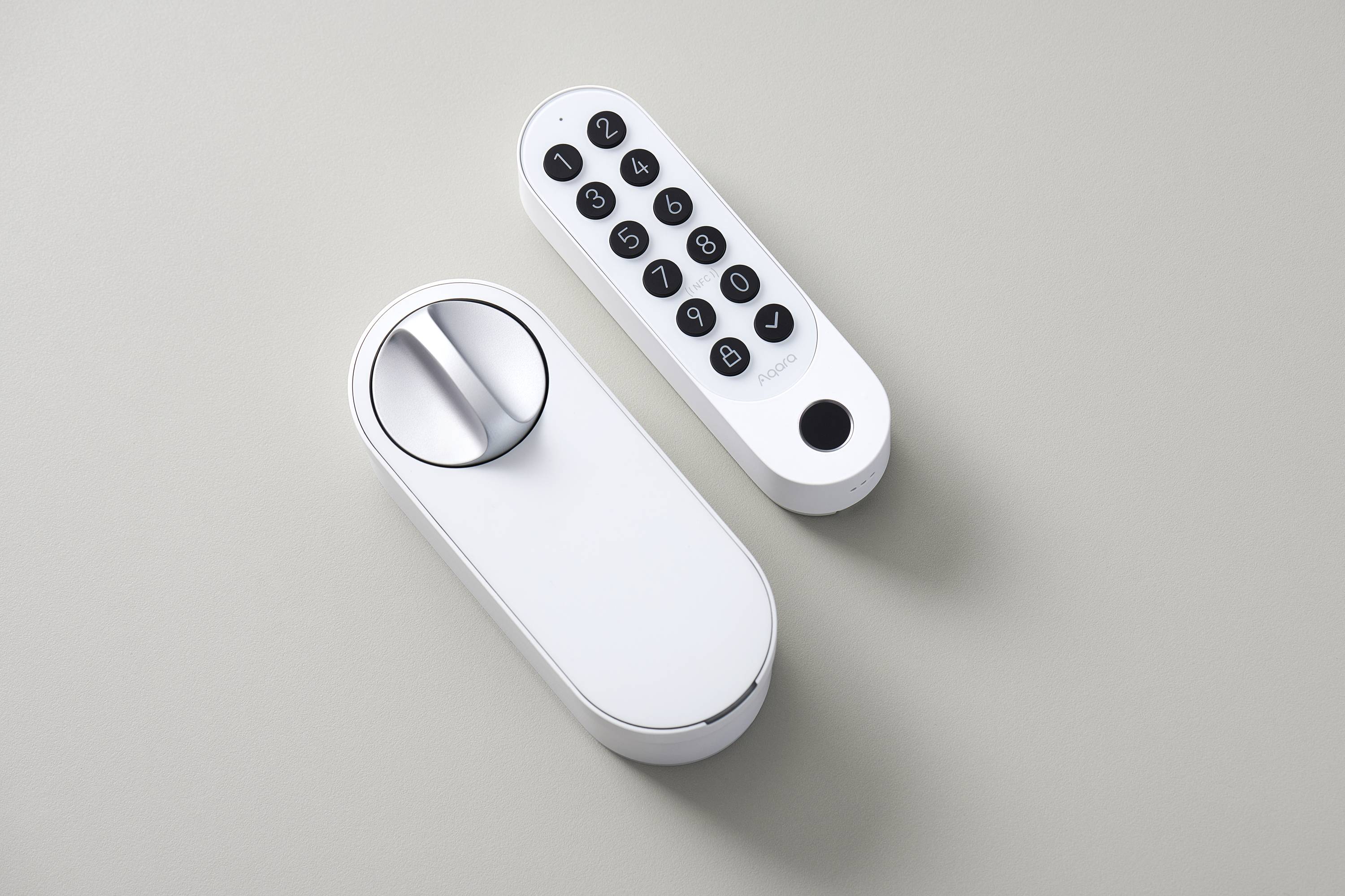 Elektronička brava za vrata s posebnom tipkovnicom za unos šifre. Oba uređaja su bijela i nalaze se na sivoj podlozi.