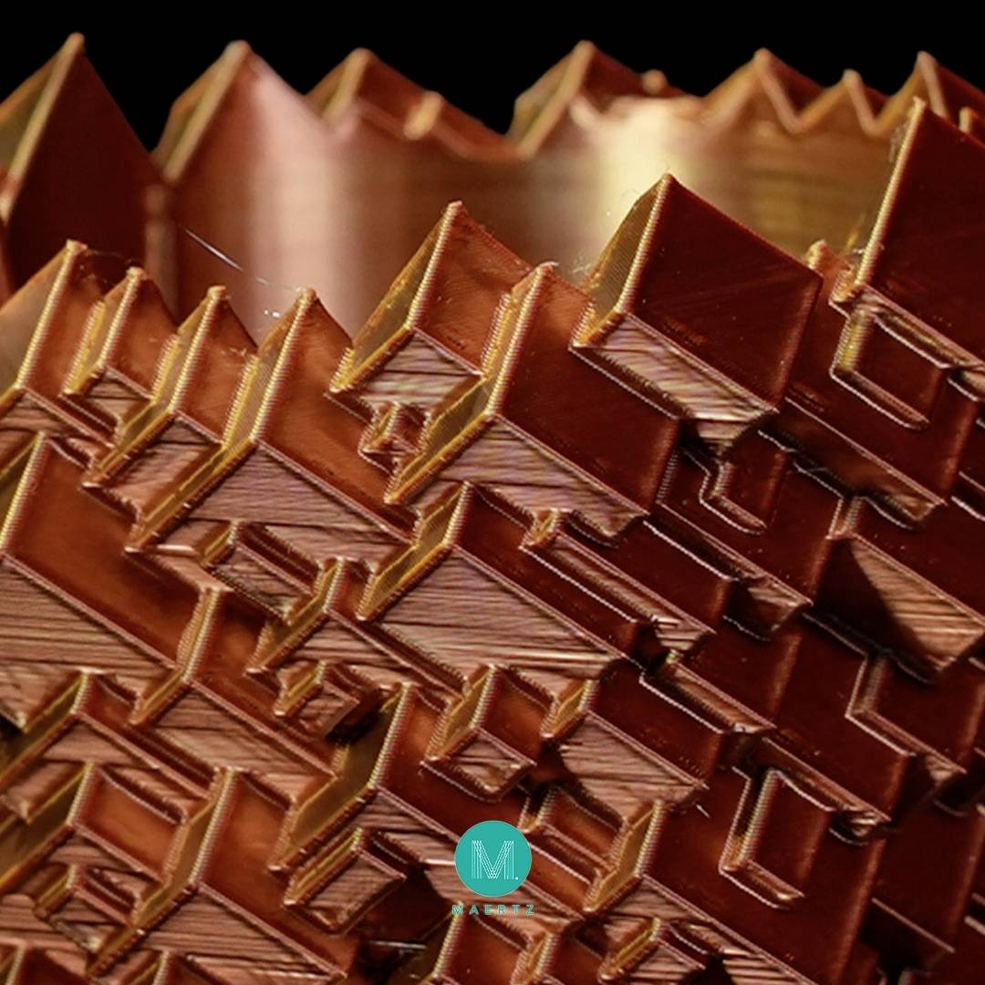 Snimka iz blizine složenog geometrijskog uzorka u bakrenoj boji izrađenog 3D printanjem.