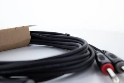 Crni audio kabel s dva priključka, smotana na stolu. Jedan priključak ima crveni prsten, drugi crni.
