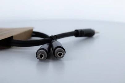 Crni audio kabel s dva ženska priključka i jednim muškim utikačem leži na stolu. U pozadini je ambalaža.