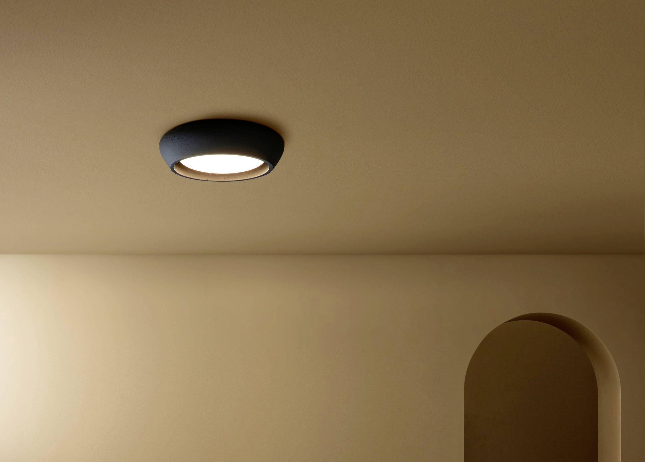 Stropna lampa u prostoriji s krem zidovima i lukasto postavljenim prolazom. Minimalistički dizajn s blagom svjetlošću.