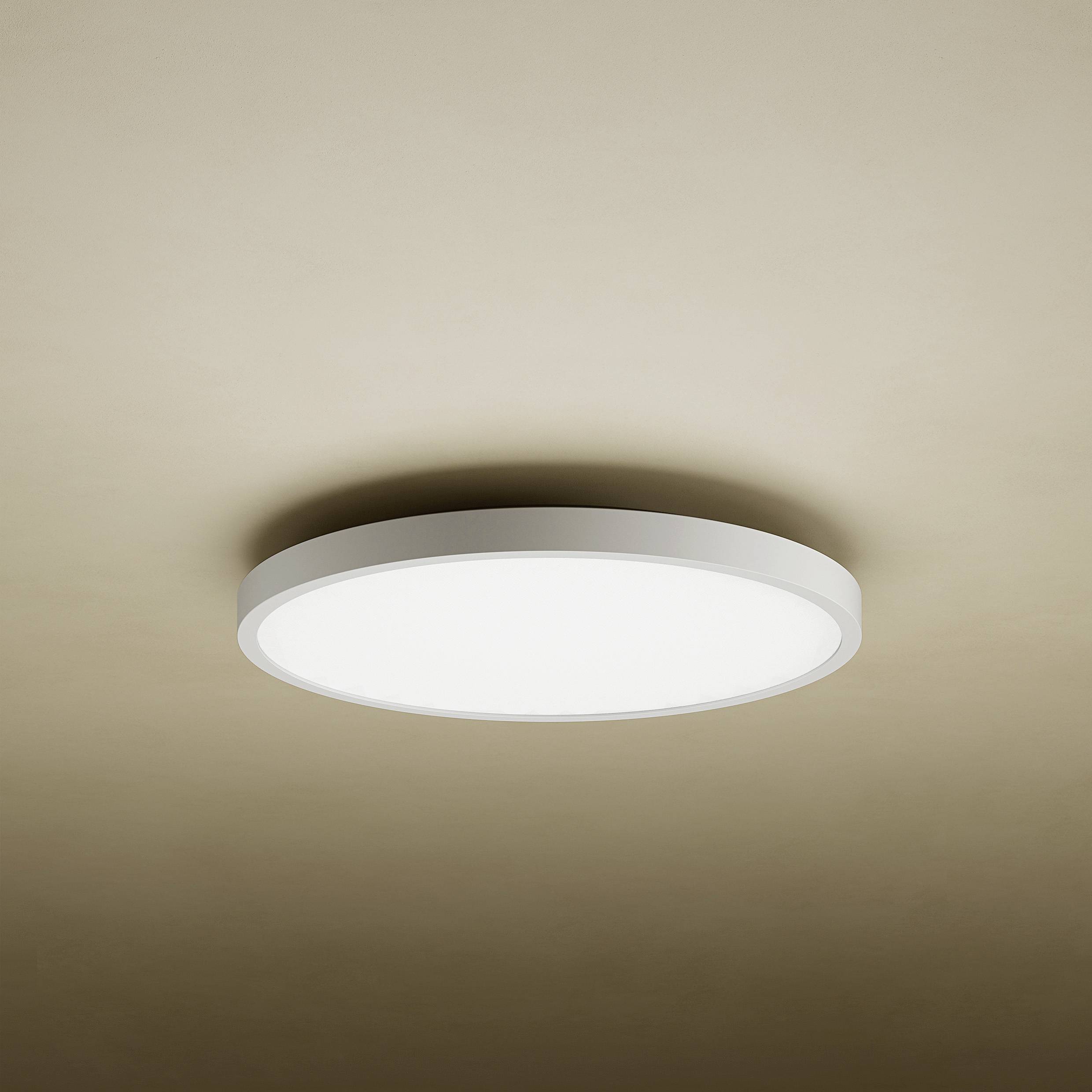 Okrugla stropna svjetiljka koja daje ravnomjerno, meko svjetlo na bež stropu. Minimalistički dizajn, moderan i elegantan.