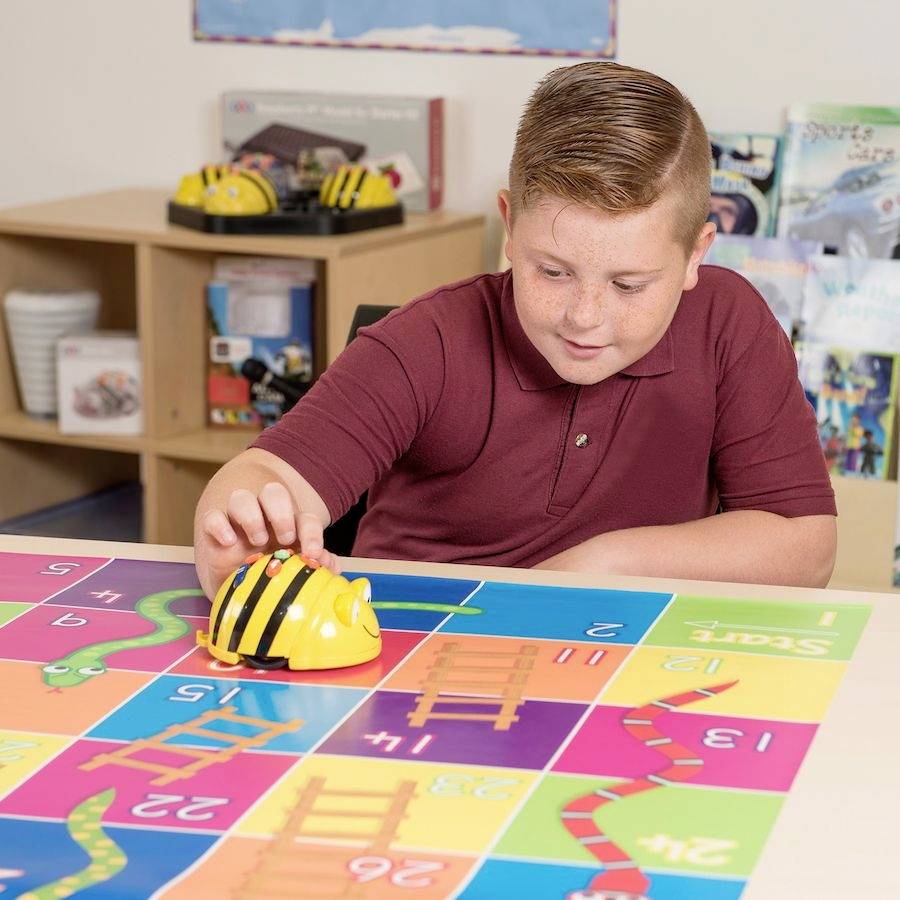 Dijete se igra malenim robotom u obliku pčele na šarenoj ploči s brojevima i simbolima ljestava.