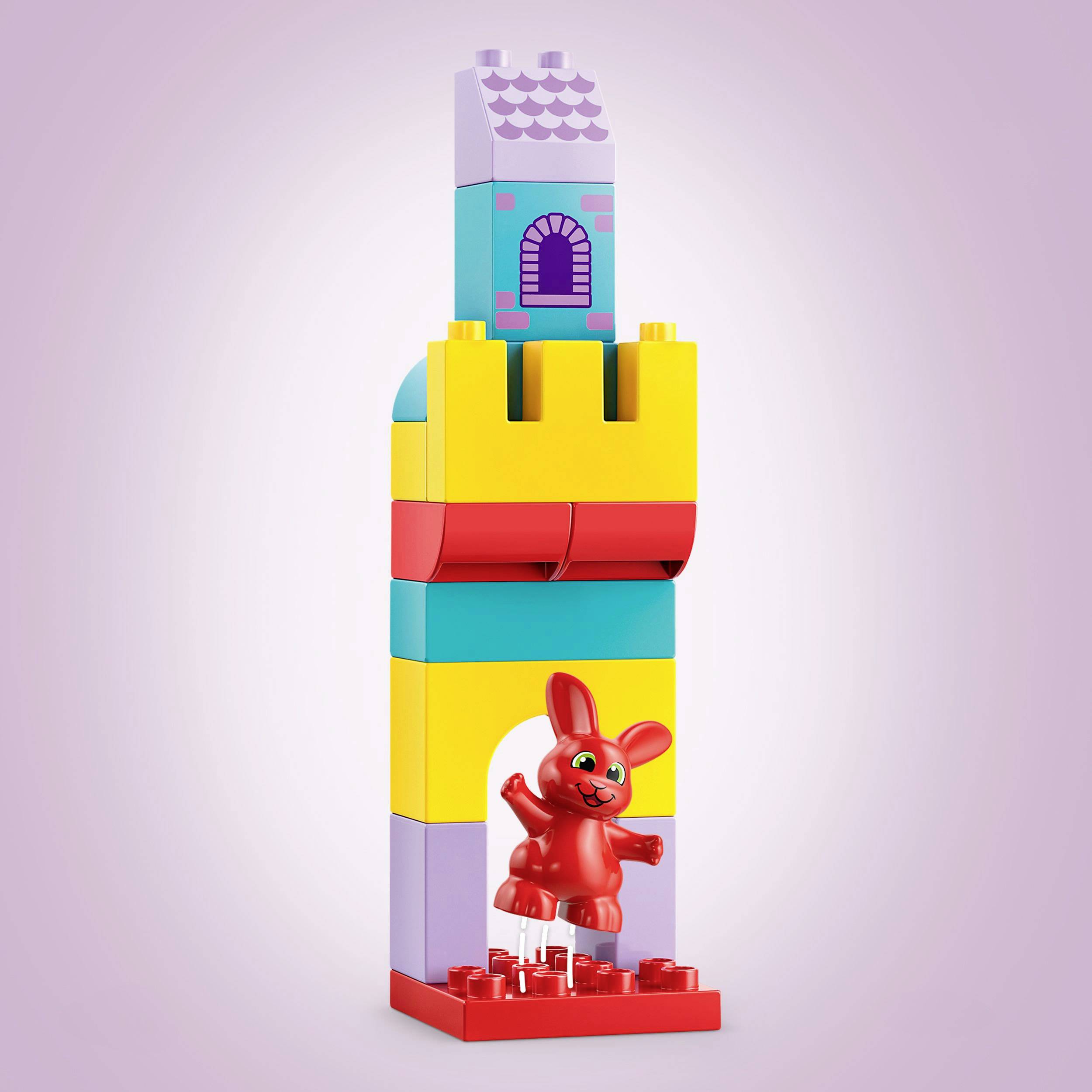 Šareni Lego toranj s ljubičastim vratima i prozorskim elementom iznad njih. Crveni zec stoji pred vratima na crvenoj postolju.