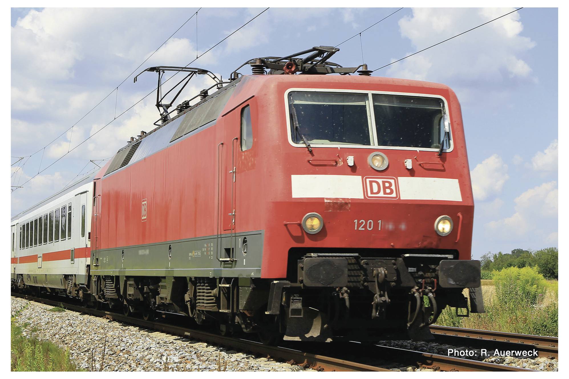 Crveni InterCity vlak Deutsche Bahn vozi željezničkom prugom kroz ruralni krajobraz. Nebo je vedro i sunčano.