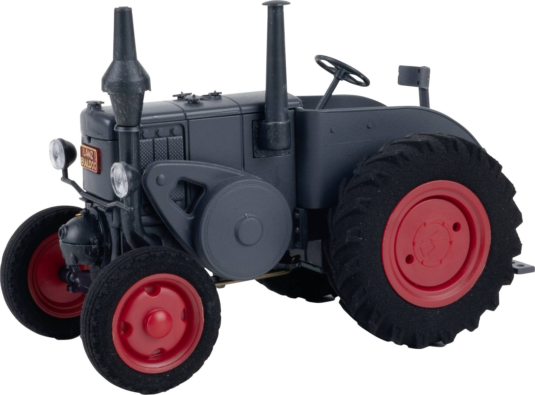 Sivi traktor s crvenim kotačima stoji na bijeloj pozadini. Ima dva vertikalna ispušna cijevu i jednostavnu upravljačku ručku.
