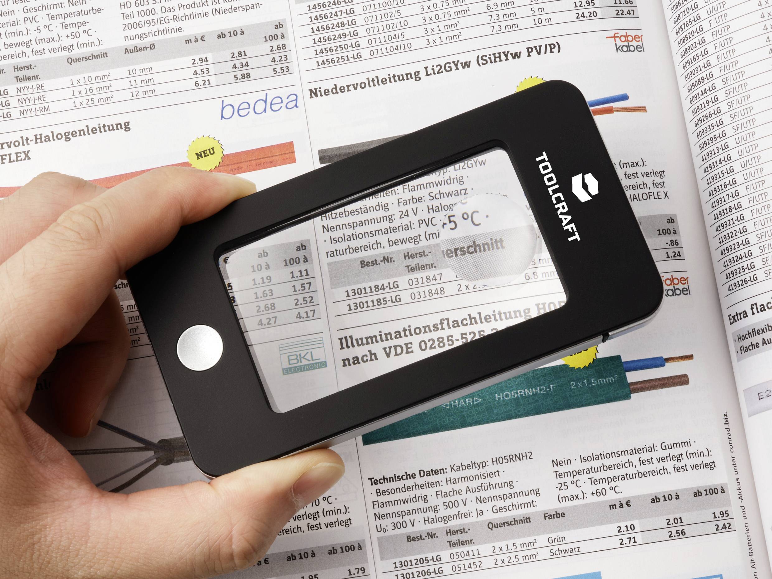 Ruka drži povećalo iznad stranice kataloga, povećavajući tekst o elektroničkim komponentama. Stranica sadrži grafikone i tehničke specifikacije.