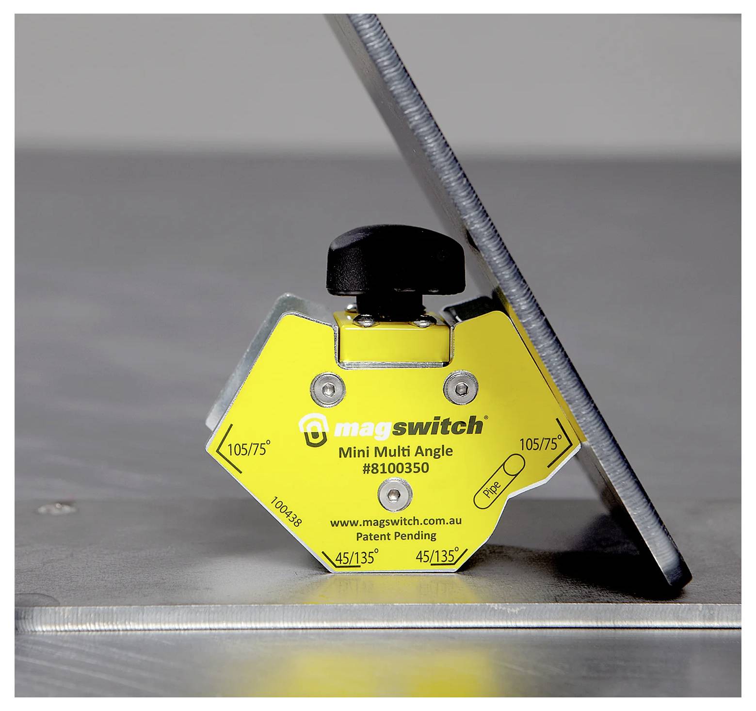Žuti Magswitch Mini Multi Angle magnet drži metalnu ploču pod kutom na metalnoj površini, prikazujući svoju funkcionalnost.