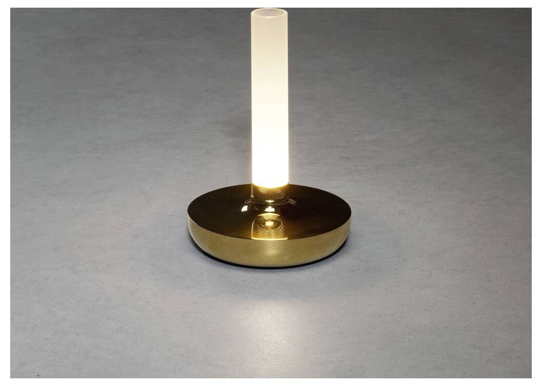 Moderna stolna lampa s cilindričnim mliječnobijelim staklenim žaruljom na okrugloj mesinganoj bazi, koja emitira meko svjetlo na sivoj površini.