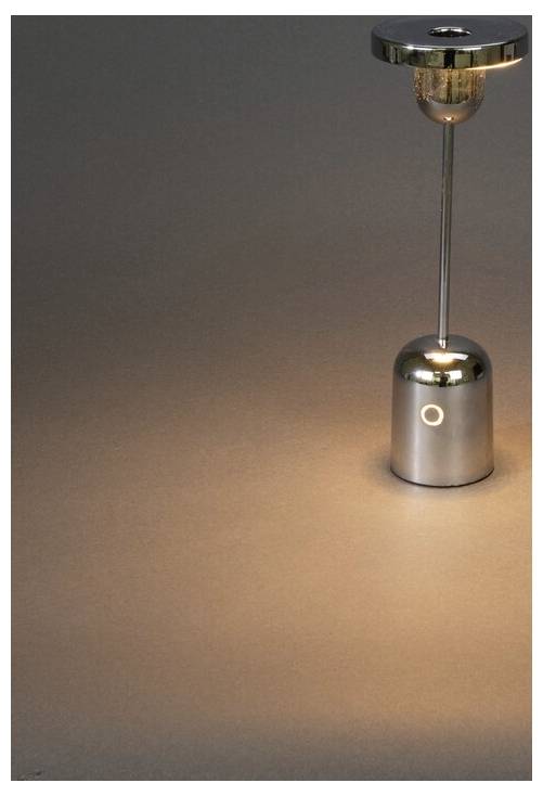 Elegantna, moderna srebrna lampa s cilindričnom bazom i kružnim svjetlosnim tijelom baca topli sjaj na neutralnu površinu.
