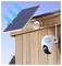 Solarni panel postavljen na drvenom zidu napaja sigurnosnu kameru smještenu ispod njega, demonstrirajući ekološki prihvatljiv sustav nadzora.