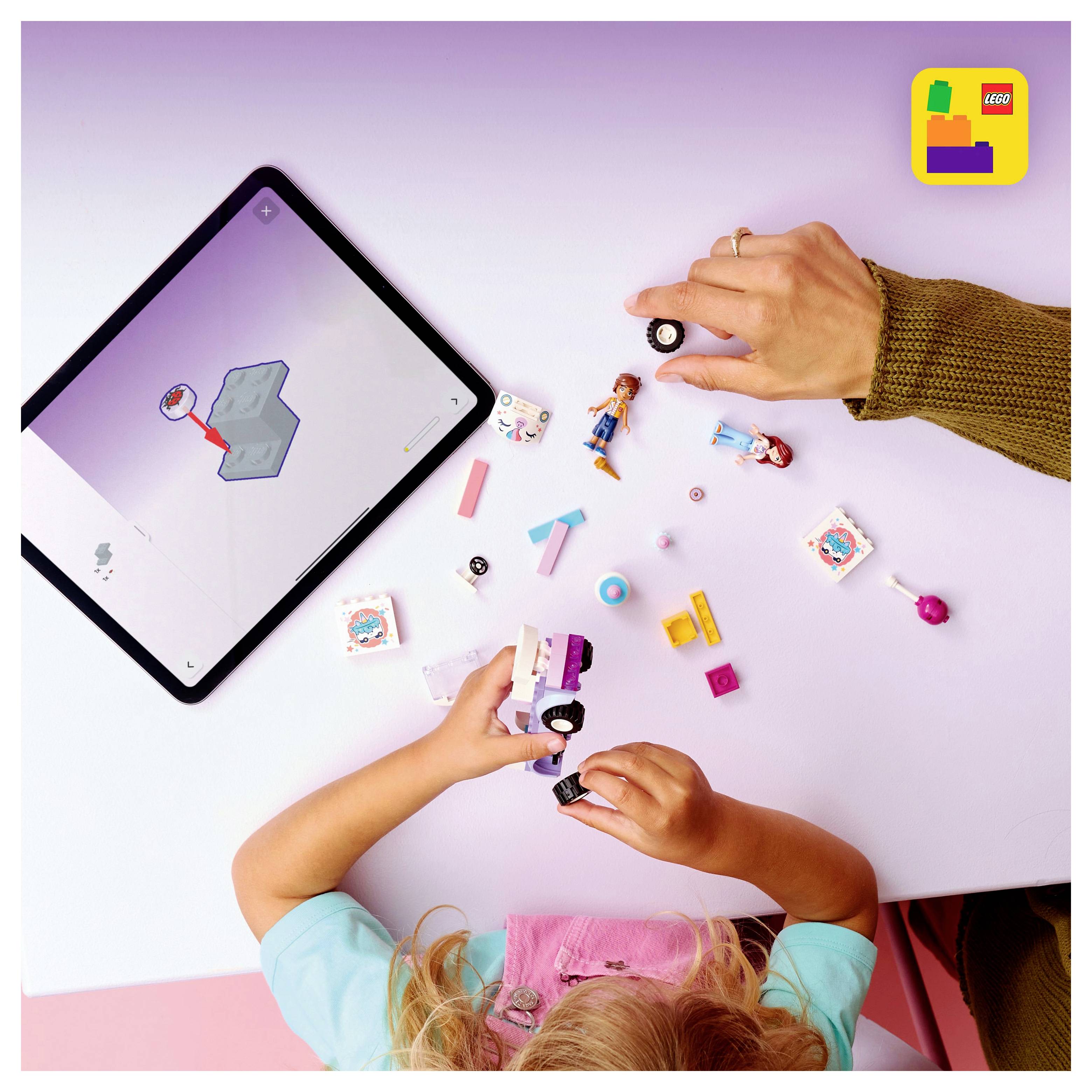 Dijete koje igra s LEGO setom na ružičastom stolu, sastavljajući vozilo dok slijedi upute na tablet zaslonu sa strane.