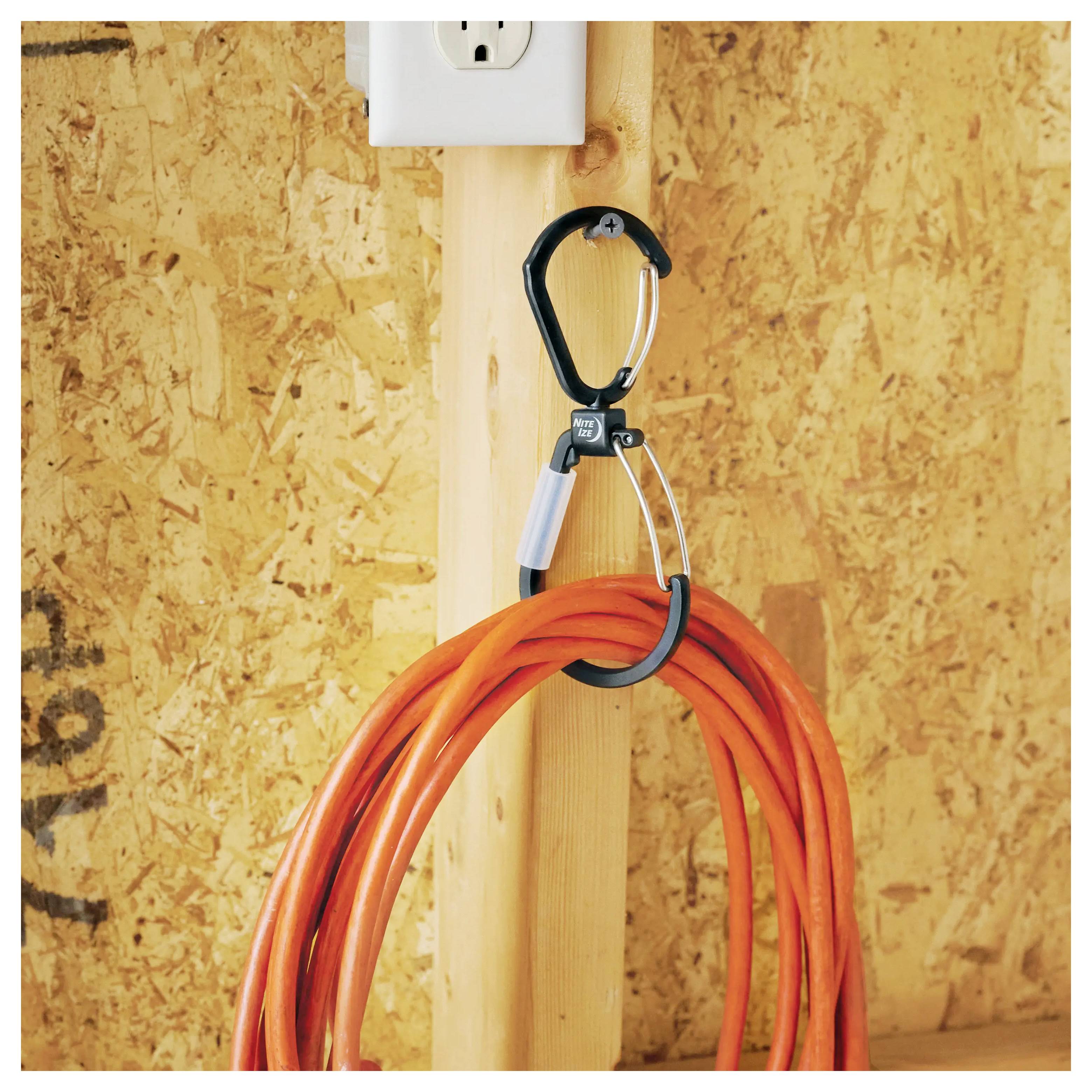 Narančasti produžni kabel je uredno namotан i obješen na kuku pričvršćenu za drvenu dasku, pored električne utičnice.