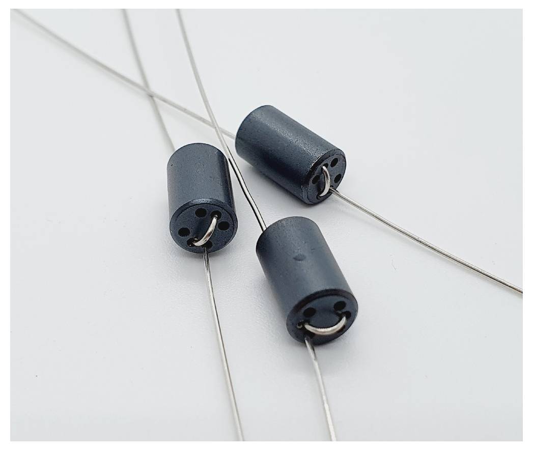 Tri cilindarska feritna prstena s metalnim vodičima koji leže na bijeloj podlozi, korišteni za prigušivanje električnih smetnji u strujnim krugovima.