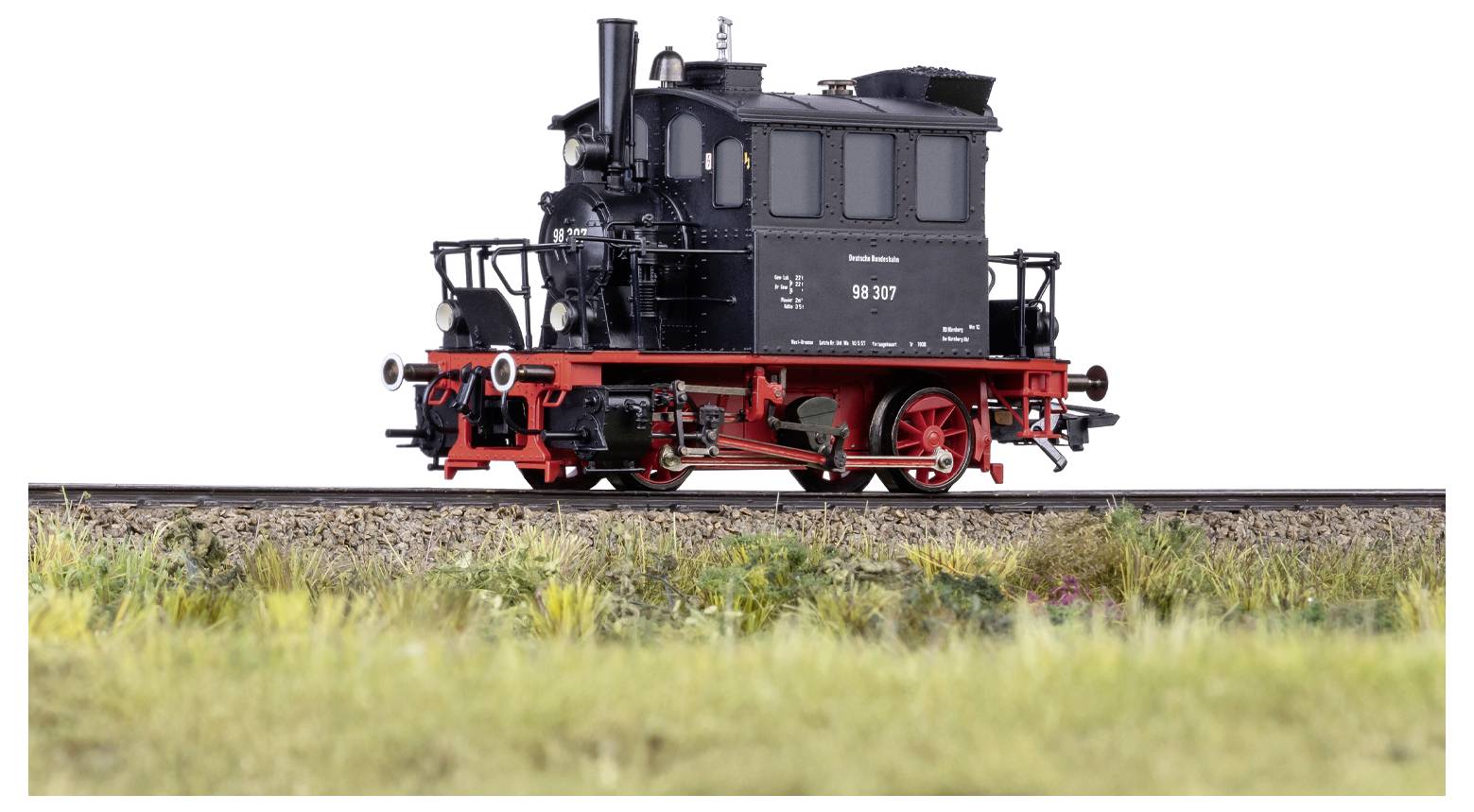 Model minijaturne crne parne lokomotive na pruzi, snimljen sa strane, koji prikazuje detaljne značajke uz travnatu pozadinu u prednjem planu.