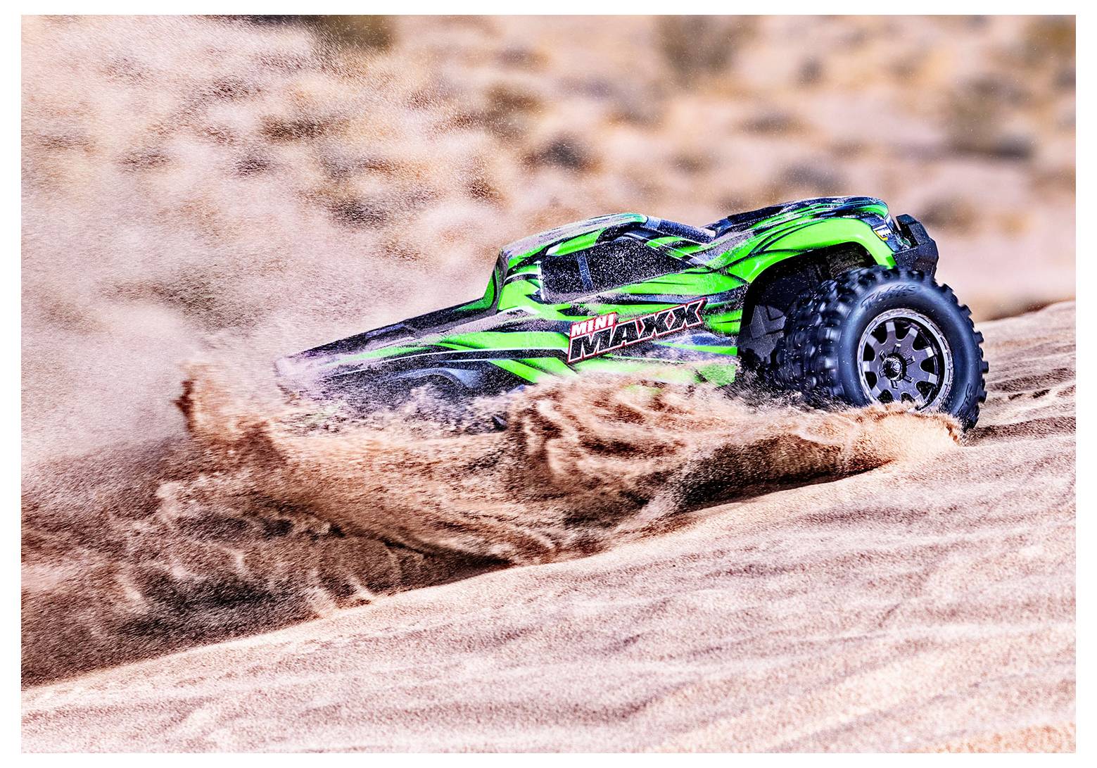 Daljinski upravljani monster truck zeleno-crnog dizajna vozi kroz pijesak, podižući oblak prašine u vanjskom prostoru.