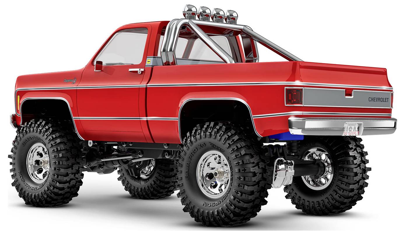 Crveni off-road kamion s velikim gumama i kromiranim detaljima, parkiran na bijeloj pozadini, koji prikazuje njegovu robusnu izvedbu i modifikacije.