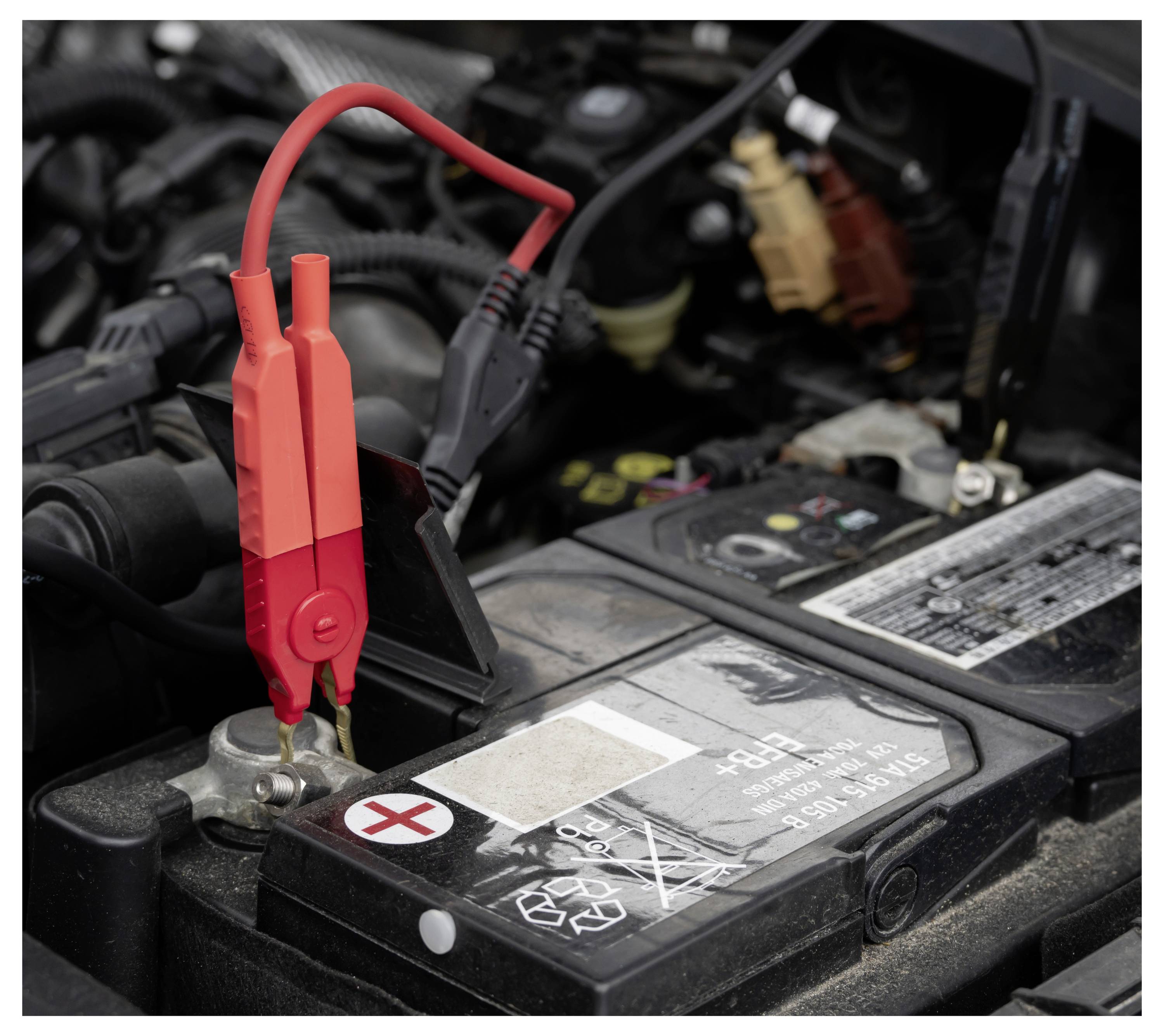 Crveni kablovi za pokretanje prikačeni na auto bateriju u motornom pretincu, što ukazuje na pokretanje vozila strujom ili punjenje baterije.