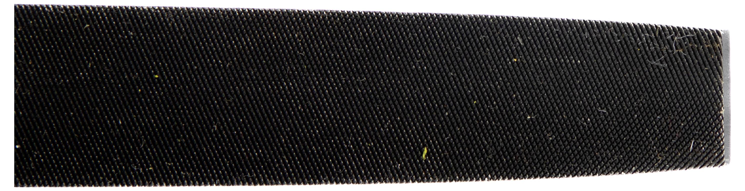 Bliskopalna slika grube, tekstuirane površine koja nalikuje pilom ili abrazivnom materijalu, prikazujući sitne žljebove i čestice na tamnoj pozadini.