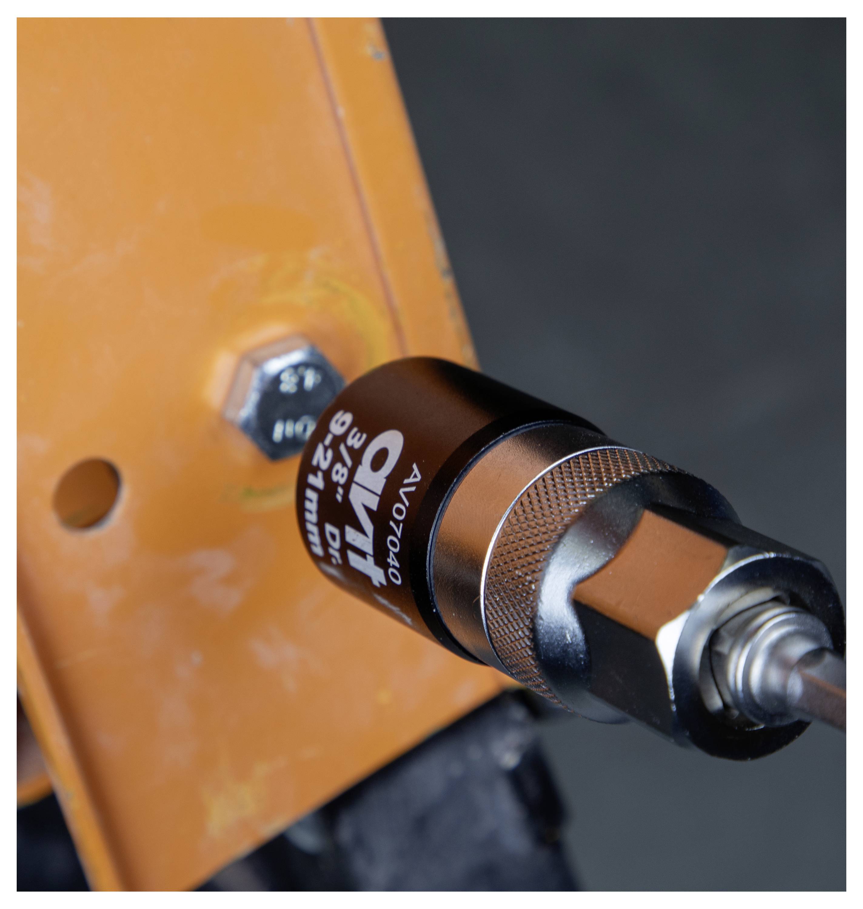 Detaljan prikaz industrijskih alata spojenih na narančasti metalni okvir, pritegnut vijak. Alat ima metalično i crno telo.