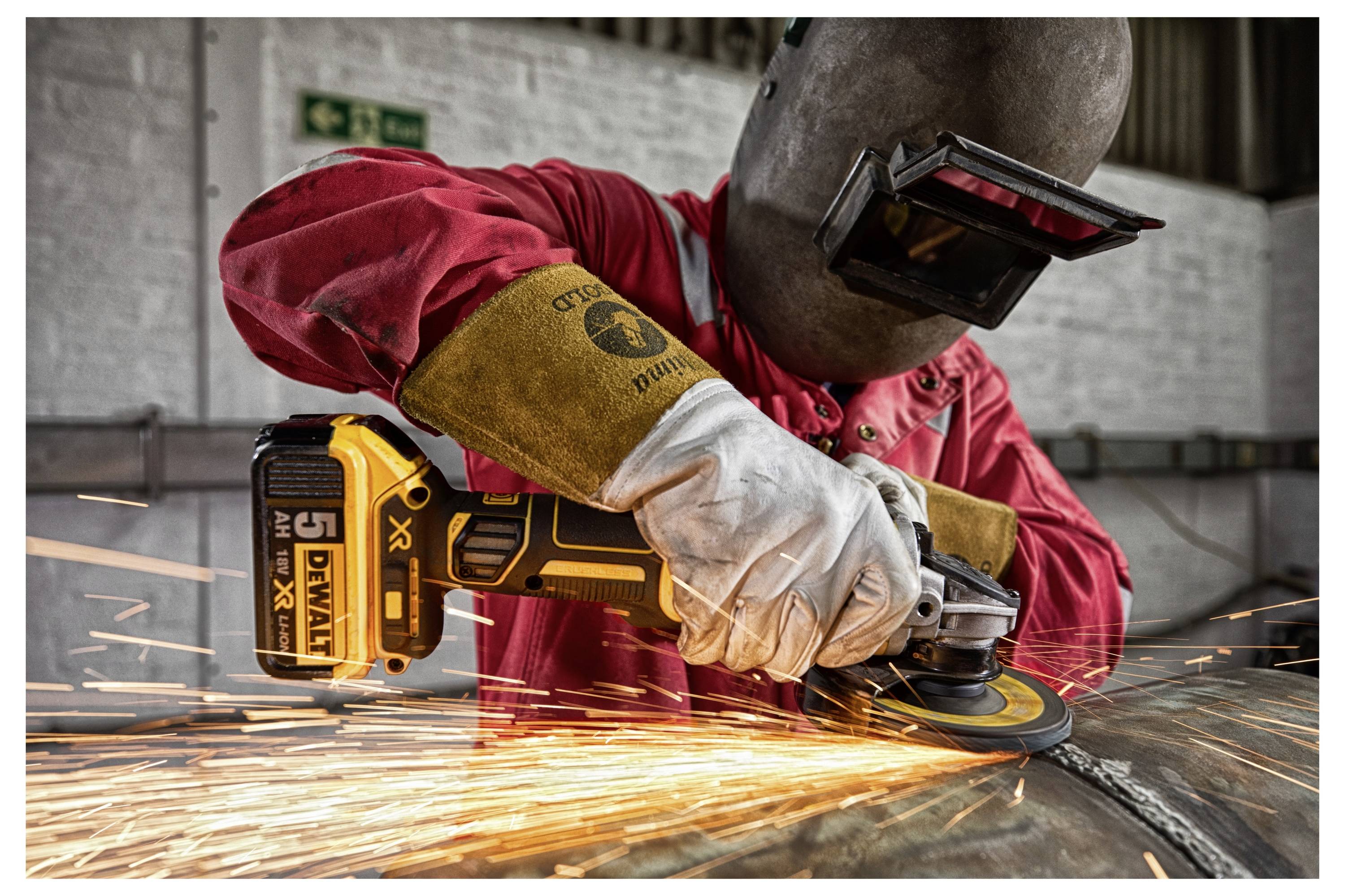 Osoba u zaštitnoj opremi koja koristi kutnu brusilicu, iskre lete od metala, prikazujući industrijski rad i mjere sigurnosti.