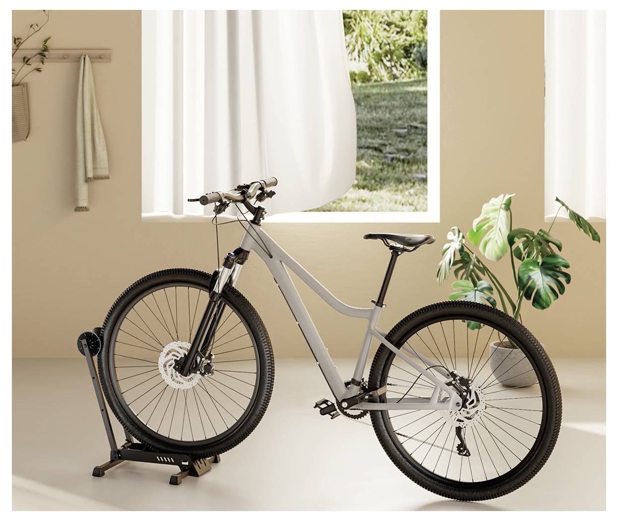 Elegantna siva cestovna bicikla montirana na stojaču za indoor trening u toplo osvijetljenoj sobi sa zelenim biljkom i prozorom kroz koji se vidi zelenilo vani.