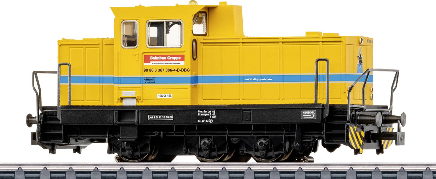 Žuti model lokomotive s plavom prugom, označen s 'Bahnbau Gruppe' na boku, prikazan na tračnicama s detaljnom ogradom i kotačima.