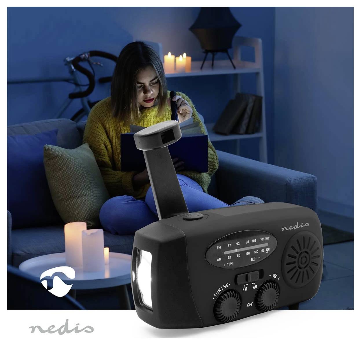 Osoba sjedi na kauču čitajući knjigu uz svjetlost svijeće. U prednjem planu prikazan je Nedis radio s baterijskom svjetiljkom i ručnom rukom za napajanje.