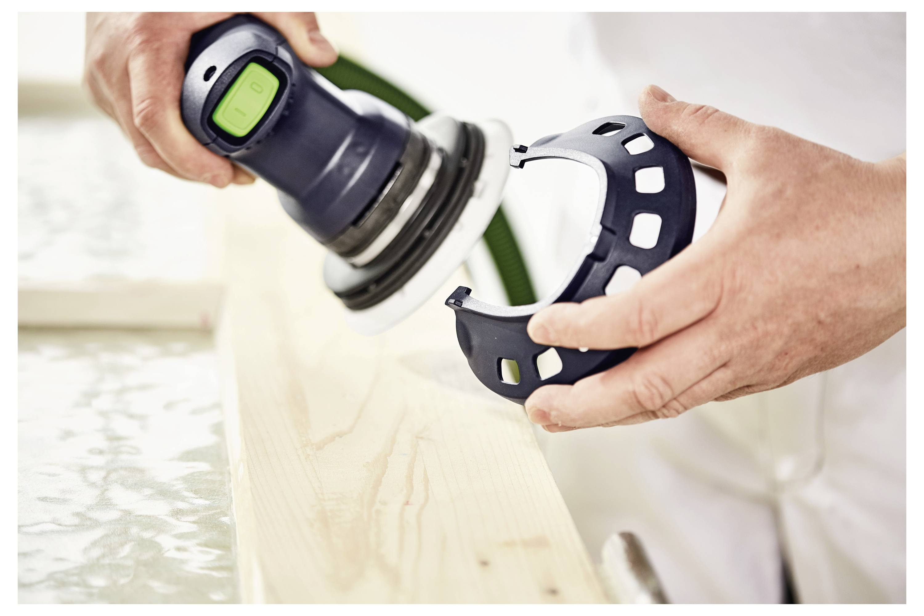 Osoba koristi okruglu ručnu brusilicu na drvenu površinu, držeći plavu zaštitnu gardulu u jednoj ruci.